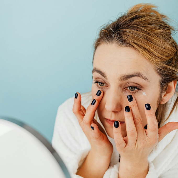 Woman looking in a mirror and applying cream under her eyes