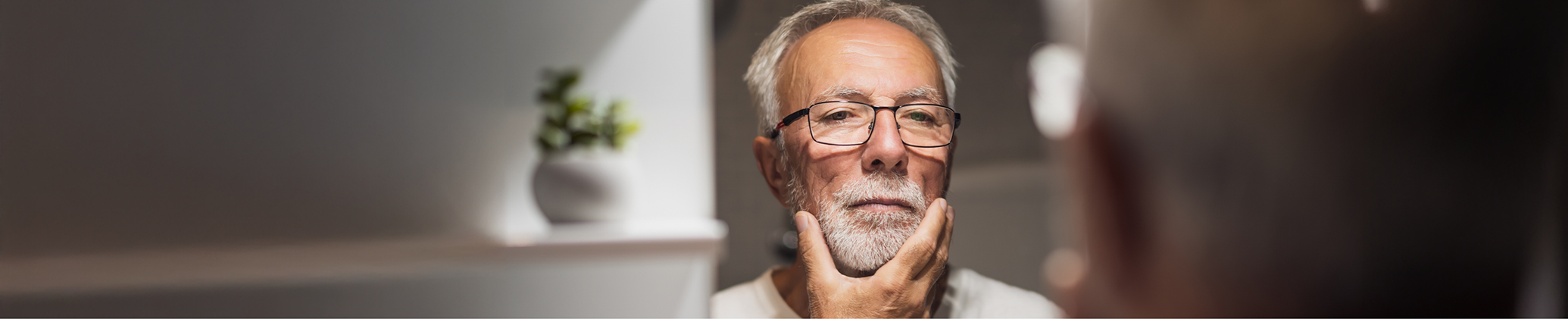 Senior man looking closely at his face in a mirror