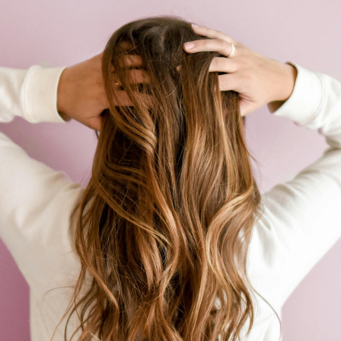 Woman seen from behind touching her long dirty blonde hair