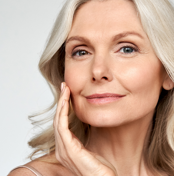 Smiling woman with long gray hair touching her face