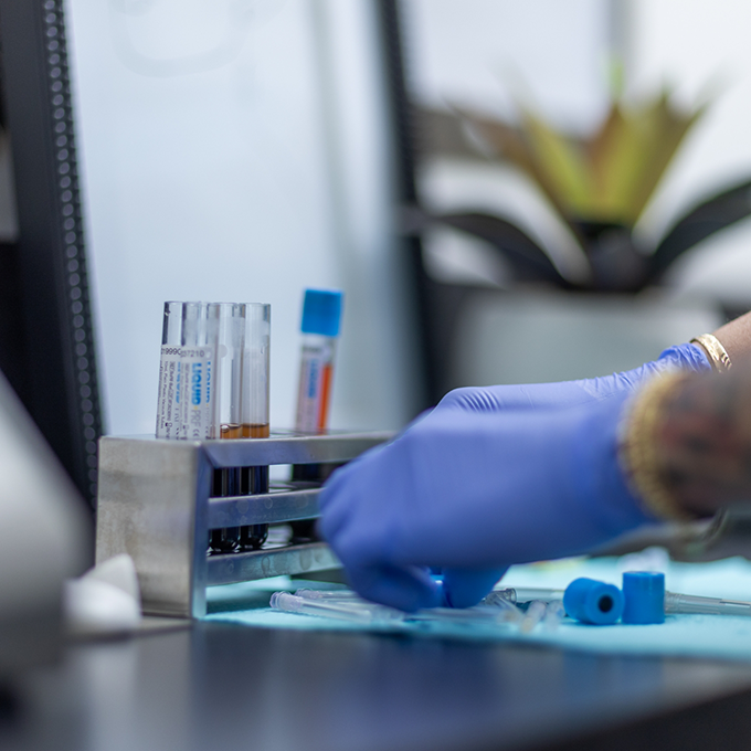 Two gloved hands adjusting tools on a desk with blood samples