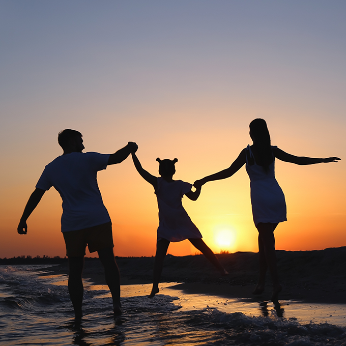 Family of three walking along the beach at sunset