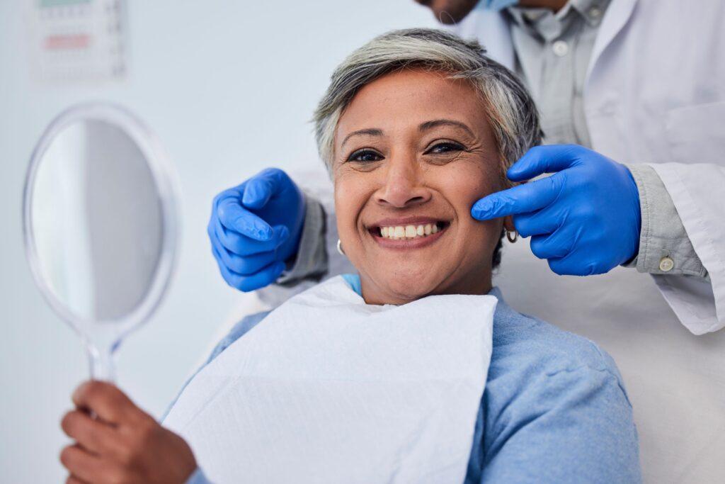 Dentist pointing to smile of woman with gray hair holding handheld mirror